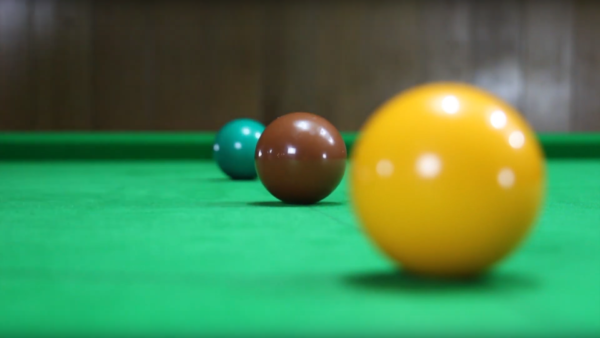 Foto einer Film-Aufnahme. Es zeigt 3 Snooker-Kugeln. Eine grüne, eine braune und eine gelbe. Die grüne und gelbe Kugel ist nicht im Fokus. Die braune Kugel ist fokussiert und scharf.